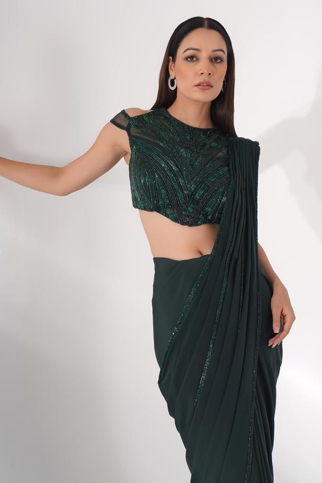 Green lycra pre-draped saree with pleated draped detail and attached embroidered pallu. Paired with padded blouse with all over tonal cut dana, pearl and bead embroidery.
Components: 2
Pattern: Embroidered
Type Of Work: Bead, Stone, and Cut Dana Work
Neckline: Closed Neck
Sleeve Type: Cold Shoulder Sleeves
Fabric: Lycra
Color: Green
Other Details: 
Embroidered sheer back
Pointed blouse hem
Saree Length: 44 inches
Occasion: Cocktail,Sangeet - Aza Fashions Draped Fitted Choli For Party, Fitted Evening Blouse With Cape Sleeves, Fitted Draped Evening Choli, Fitted Green Choli For Evening Wear, Fitted Green Choli For Evening, Fitted Blouse With Cape Sleeves For Reception, Embellished Fitted Draped Choli, Evening Blouse With Sequins In Traditional Drape, Evening Georgette Tops With Sequins