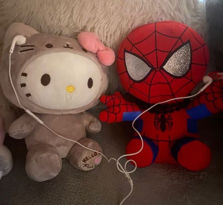 two hello kitty stuffed animals next to each other on a couch with a spiderman plush toy