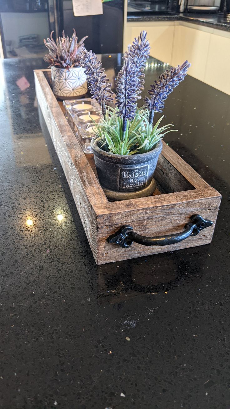 two potted plants sitting on top of a wooden box in the middle of a kitchen