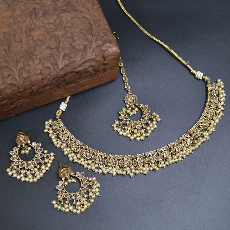 Set includes- 1 Necklace + 1 Pair of Earrings + 1 Headpiece ( Tikka ) Polish - Gold Metal - Brass Note-  Due to the lighting, there may be a slight variation in the color of the jewelry in the photo. Please do not hesitate to contact us with any questions or requests for personalization of the set. Traditional Cream Jewelry For Wedding, Gold Bridal Necklace With Elegant Design For Party, Elegant Beige Wedding Jewelry, Wedding Pearl Necklace In Beige, Elegant Beige Necklaces For Wedding, Beige Pearl Necklace For Wedding, Beige Pearl Wedding Necklace, Elegant Beige Necklace For Wedding, Elegant Beige Wedding Necklace