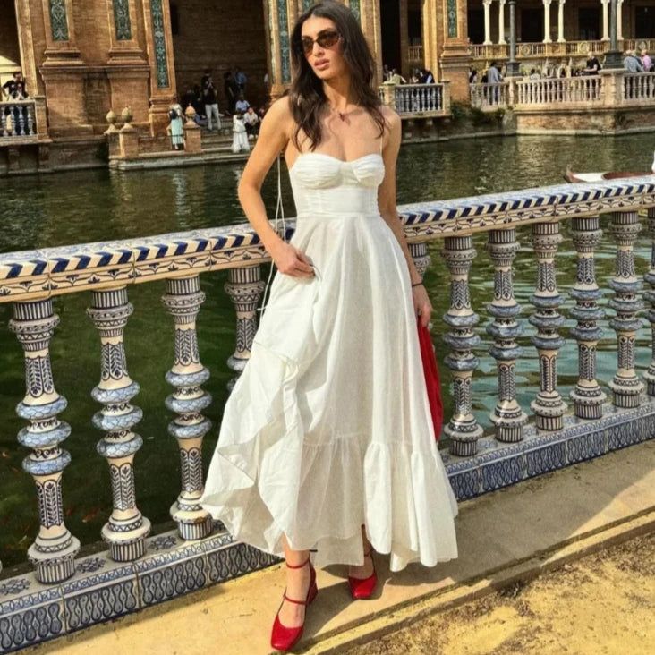 a woman in a white dress standing on a bridge next to a body of water