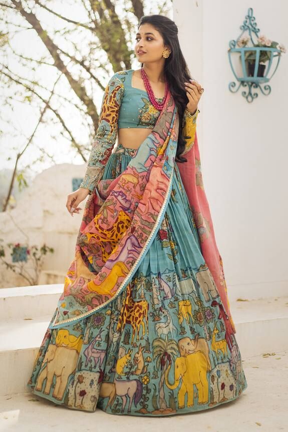 a woman in a blue and yellow lehenga with elephants on the skirt, standing outside