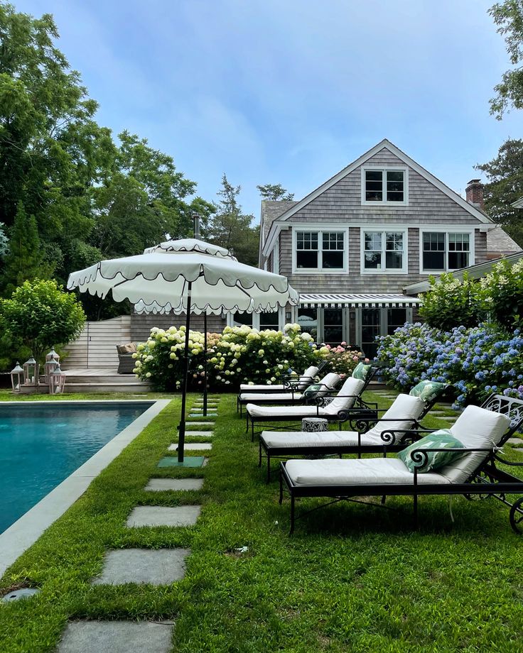 lawn chairs and umbrellas near a pool in front of a house