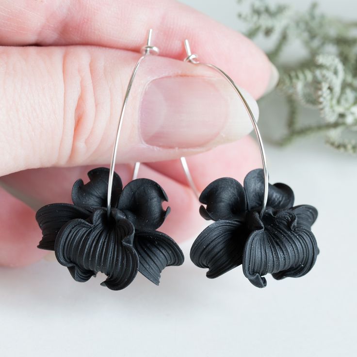 a pair of earrings with black flowers hanging from it's sides, in front of a white background