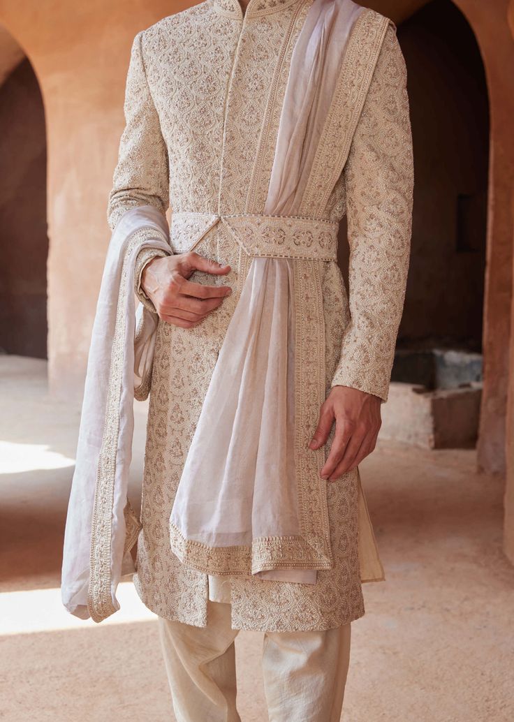 Editor's Note Exude understated luxury in our light beige raw silk sherwani, adorned with tonal resham embroidery enhanced by delicate dabka and beadwork throughout. Paired seamlessly with a monga tussar kurta and churidar, this ensemble perfectly blends traditional craftsmanship with modern elegance. A choice that radiates sophistication and charm for your special occasion. Note: Stole and belt are for styling purposes only. Fabric: Raw silk and matka tussar Color: Beige Components: Sherwani, k Raw Silk Bandhgala For Reception At Eid, Eid Bandhgala In Raw Silk For Reception, Eid Reception Bandhgala In Raw Silk, Raw Silk Unstitched Suit With Naqshi For Wedding, Wedding Unstitched Suit In Raw Silk With Naqshi, Silk Unstitched Suit With Naqshi For Wedding, Traditional Silk Churidar For Reception, Cream Churidar For Reception In Transitional Season, Cream Churidar For Reception