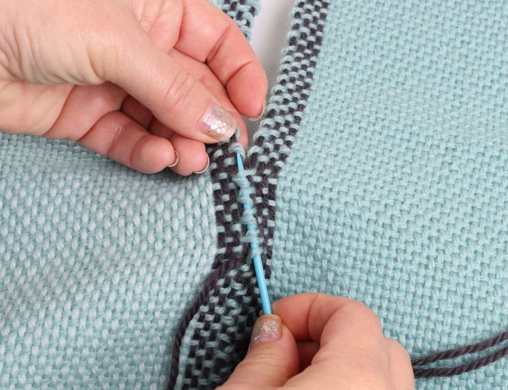 someone is knitting something on the side of a knitted sweater with a blue needle