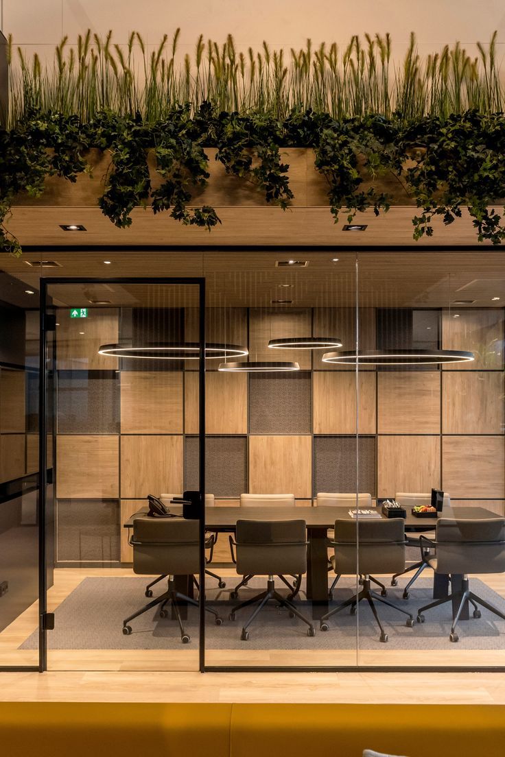 an office with glass walls and plants growing on the wall above it's desks