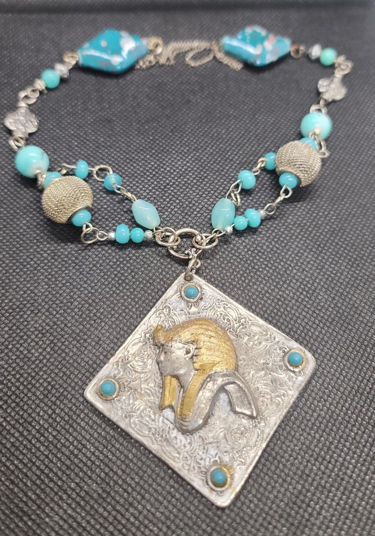 Beautiful and one of a kind, hand made silver and turquoise colored beads featured by a vintage pendant that has a unique image of an Ancient Egyptian King. The beads I used are silver,  stone, crystal and pottery.   The pendant measures 3 inches by 3 inches.   The necklace length is adjustable.  I love this necklace, I hope you will too!  Gift wrapped year round! Vintage Blue Turquoise Necklace, Vintage Beaded Turquoise Necklace As Gift, Vintage Beaded Turquoise Necklace For Gift, Handmade Bohemian Beaded Necklace For Collectors, Vintage Turquoise Pendant Necklace With Natural Stones, Vintage Turquoise Necklace With Natural Stones As Gift, Vintage Turquoise Necklace With Natural Stones For Gift, Bohemian Silver Turquoise Necklace Soldered, Handmade Antique Silver Amulet Necklace