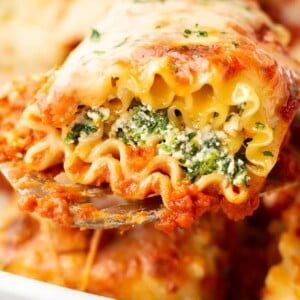 a fork full of pasta with broccoli and cheese on it is being lifted from the casserole dish