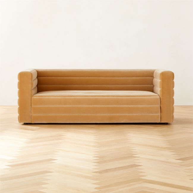 a tan couch sitting on top of a hard wood floor next to a white wall