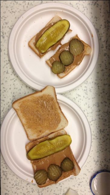 two white plates topped with sandwiches covered in peanut butter and pickle slices next to each other