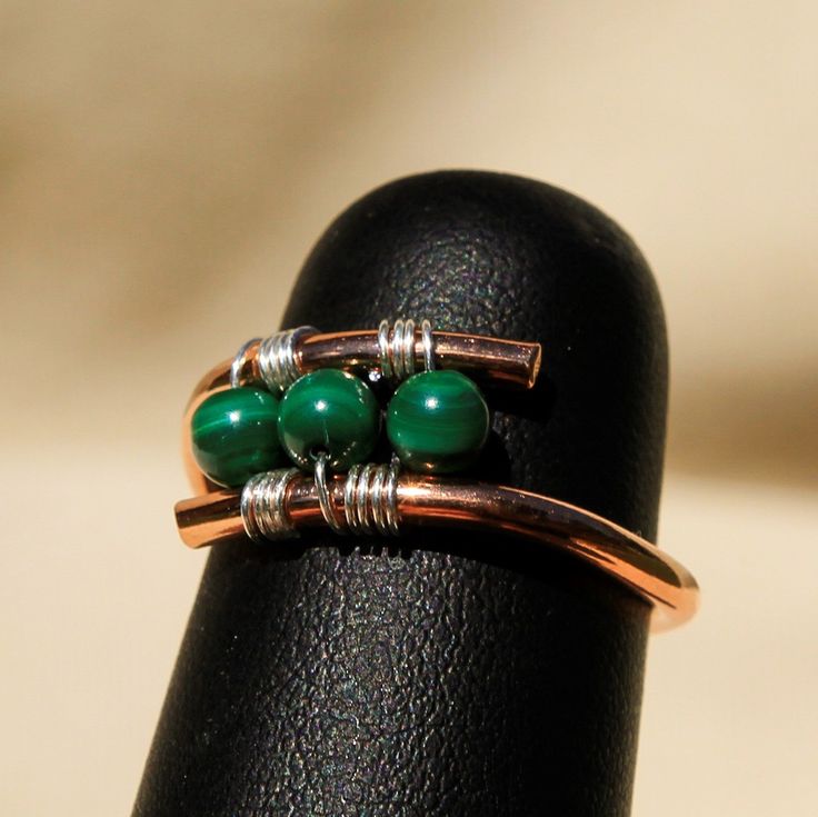 Custom shaped Copper Ring with Malachite Beads hand crafted high in the mountains of Northern New Mexico. Custom made Copper ring with Sterling Silver wire and 4mm Malachite Beads. I hand form, hand texture and metalsmith all the materials for a truly unique piece of art! Each piece is hand made - Item shipped may vary slighty from item shown in pictures. 8 oz. Shipping Weight Copper Jewelry Handmade Rings, Green Copper Rings As Gifts, Unique Green Copper Rings, Green Wire Wrapped Rings For Jewelry Making, Unique Green Copper Ring, Unique Handmade Copper Rings, Unique Green Wire Wrapped Rings, Wire Wrapped Rings Artful Home, Adjustable Copper Rings