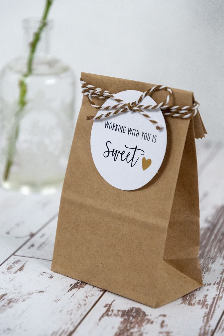 a brown paper bag sitting on top of a wooden table next to a vase filled with flowers