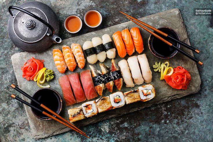 an assortment of sushi on a stone platter with chopsticks and sauce