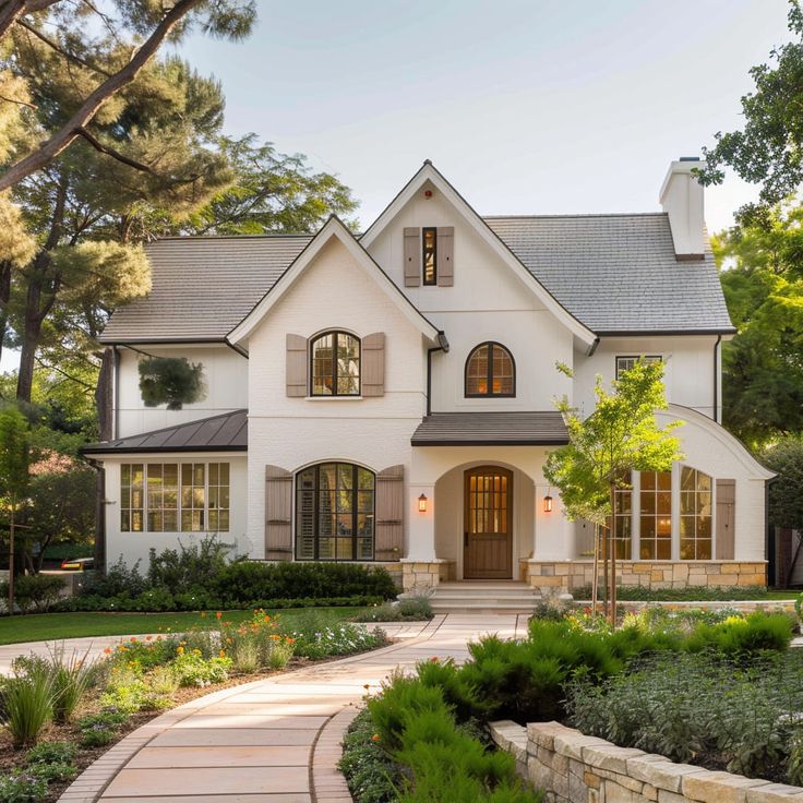 a large white house with lots of windows and plants in the front yard, surrounded by greenery