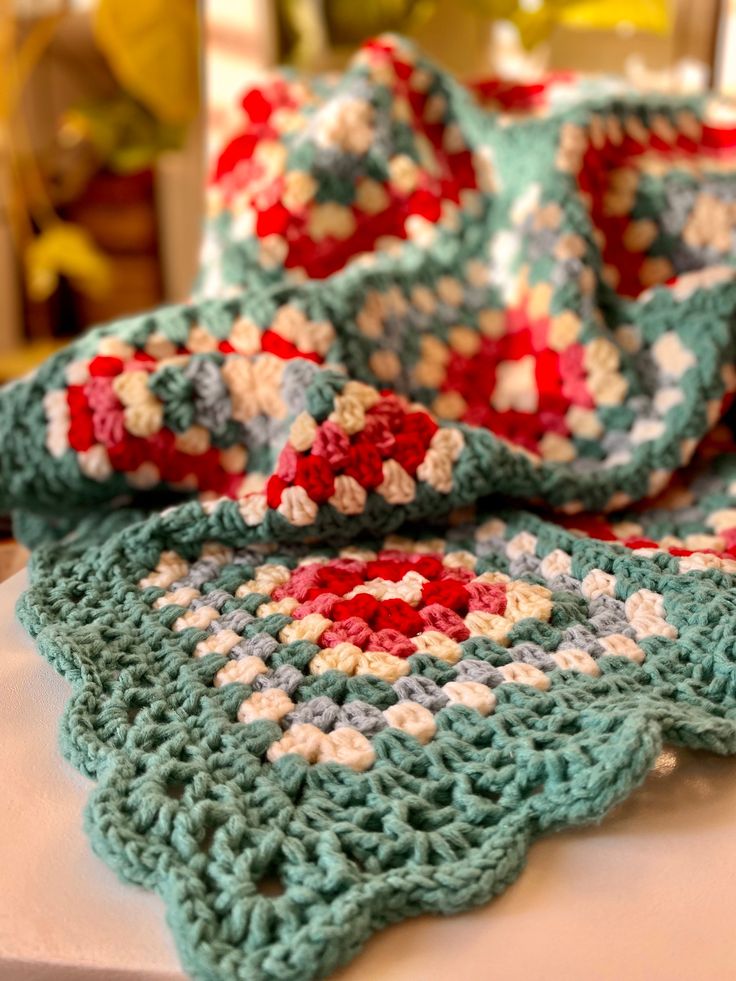 there is a crocheted blanket on top of a white table with red and blue flowers