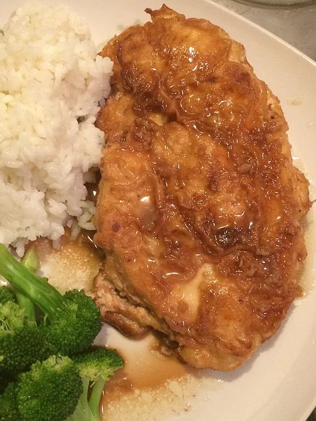 a white plate topped with meat and rice next to broccoli covered in gravy