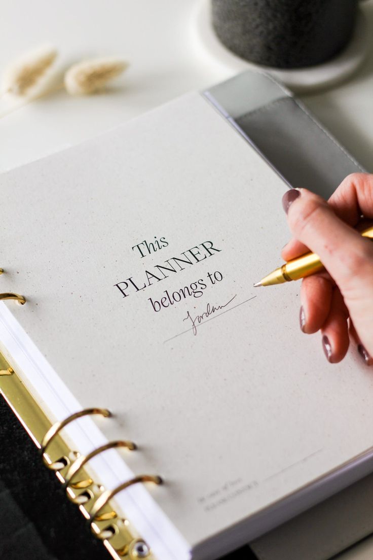 a woman's hand holding a pen and writing on a planner with the words, this planner belongs to you