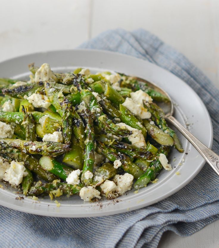 a white plate topped with asparagus covered in feta cheese on top of a blue towel