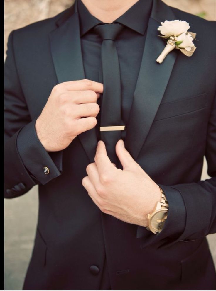 a man in a black suit adjusting his boutonniere on his lapel