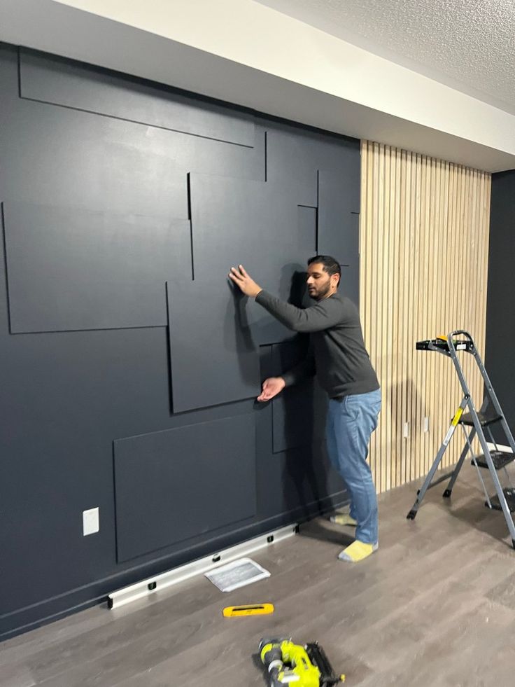 a man standing next to a black wall with some tools on the floor and one person leaning up against it