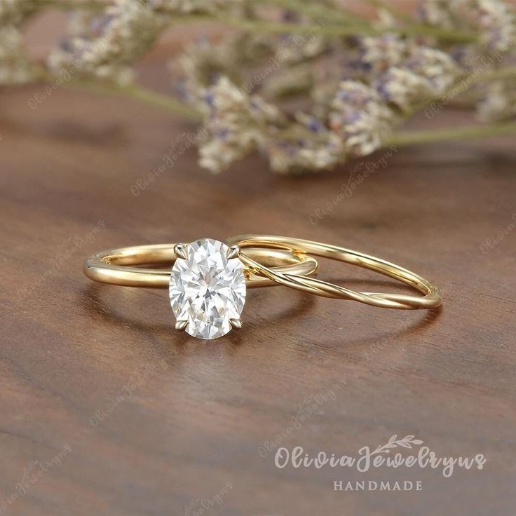 two gold rings with a single diamond on the top and one in the middle, sitting next to some lavender flowers