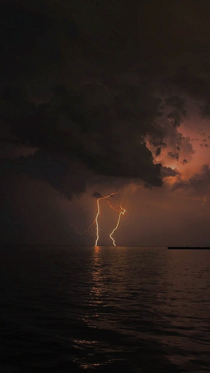 lightning striking over the ocean with dark clouds