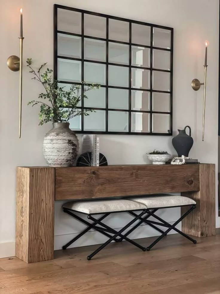 a wooden bench sitting next to a mirror and vase on top of a table in a room