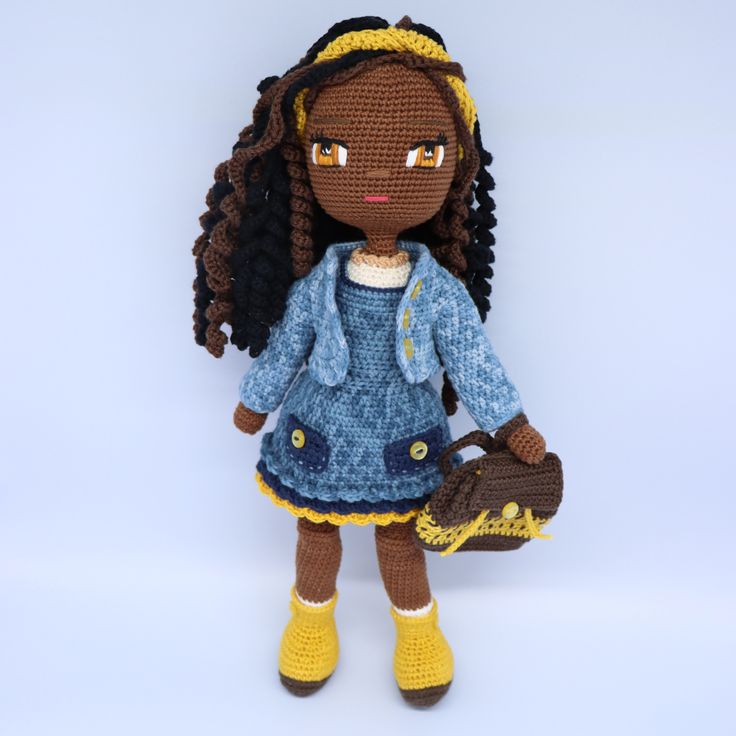 a crocheted doll wearing a blue dress and yellow shoes with her handbag