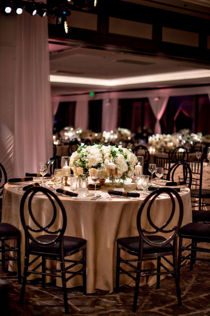 the tables are set up with white flowers and candles for an elegant wedding reception at the four corners of the room