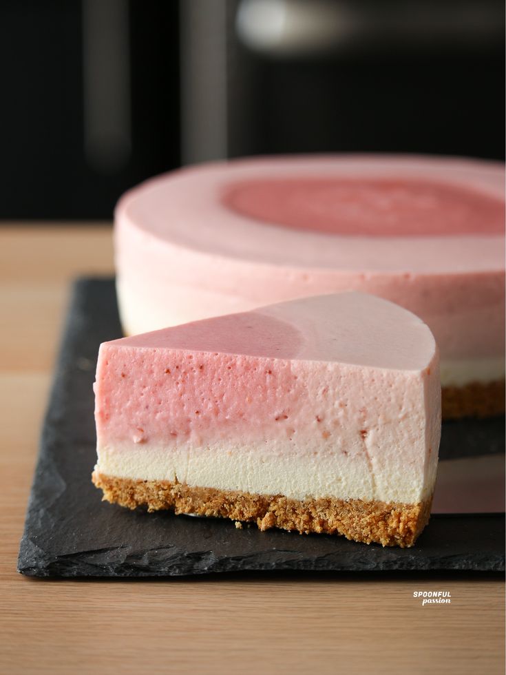 a piece of cheesecake with pink and white icing on a black slate plate