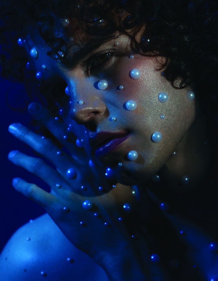 a woman's face is covered in water droplets and blue light, with her hands over her face