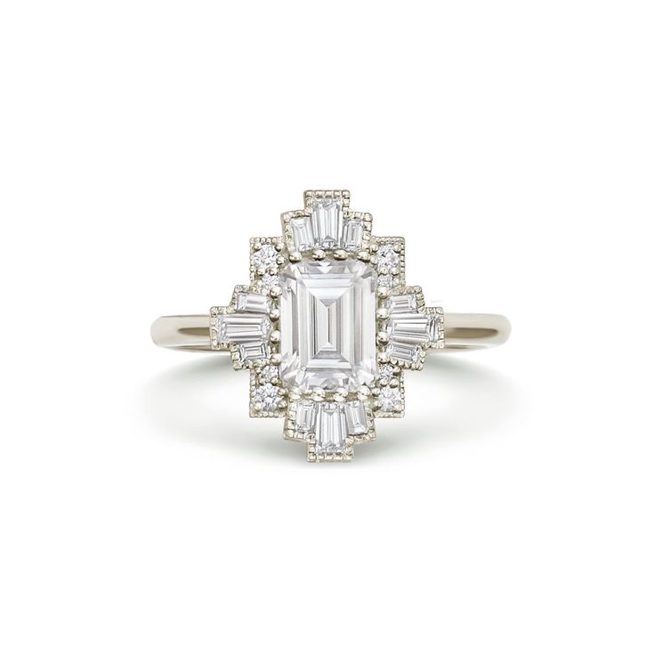 an emerald cut diamond ring with baguetts on the shoulders and side stones set in 18k white gold