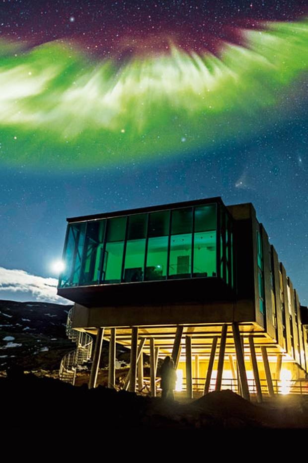 the aurora bore is lit up in the night sky over a building with people looking at it