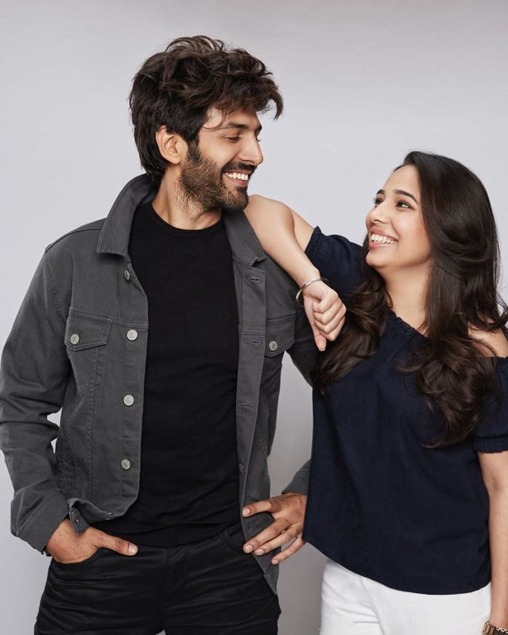 a man and woman smile at each other as they pose for a photo in front of a gray background