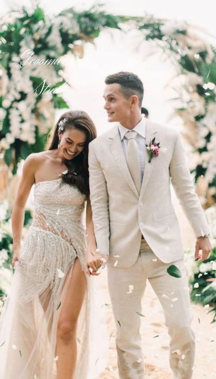 a man and woman are standing in front of an arch with white flowers on it