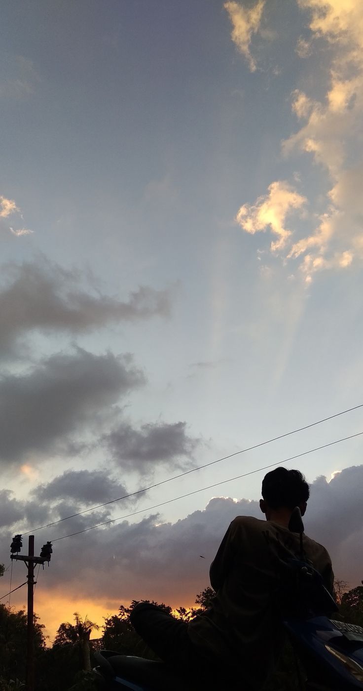 a man sitting on top of a motorcycle under a cloudy sky