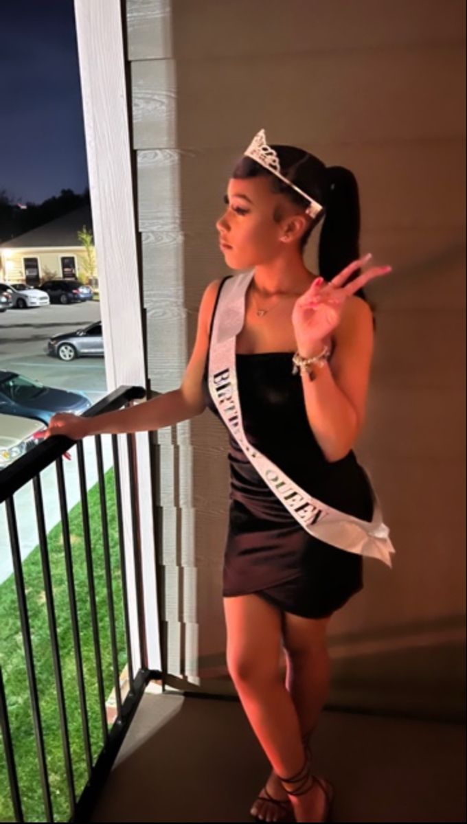 a woman standing on a porch with her hand in the air and wearing a tiara