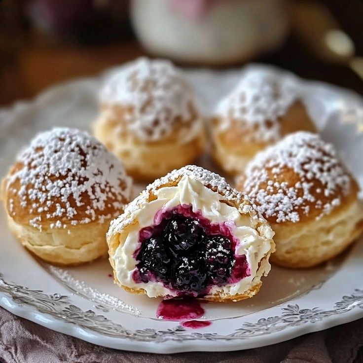 several pastries on a white plate with powdered sugar and blueberry toppings