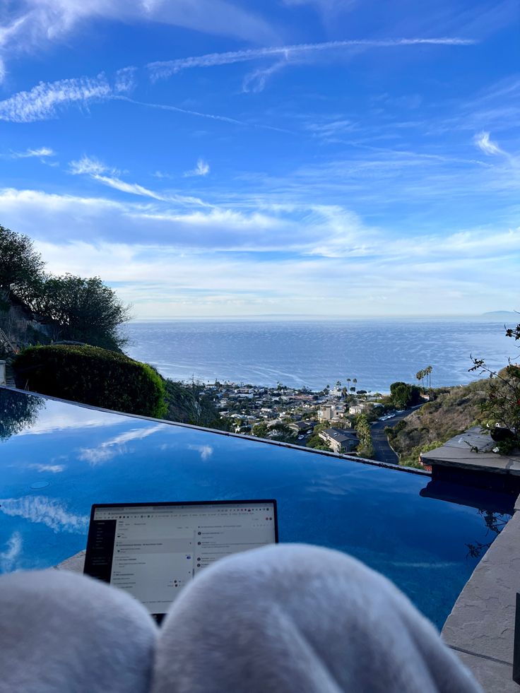 someone is looking at their laptop on the edge of a swimming pool overlooking the ocean