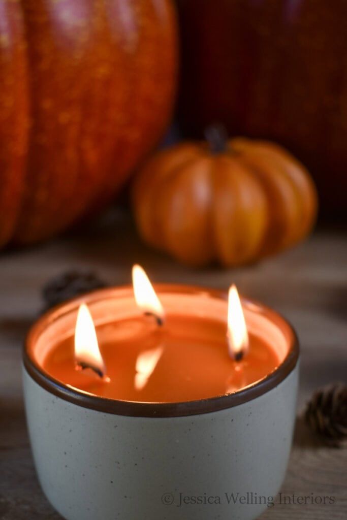 three lit candles sitting on top of a table next to pumpkins and pine cones