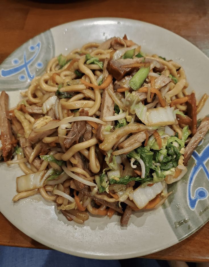 a white plate topped with noodles and veggies on top of a wooden table