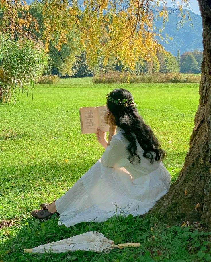 a woman sitting under a tree reading a book