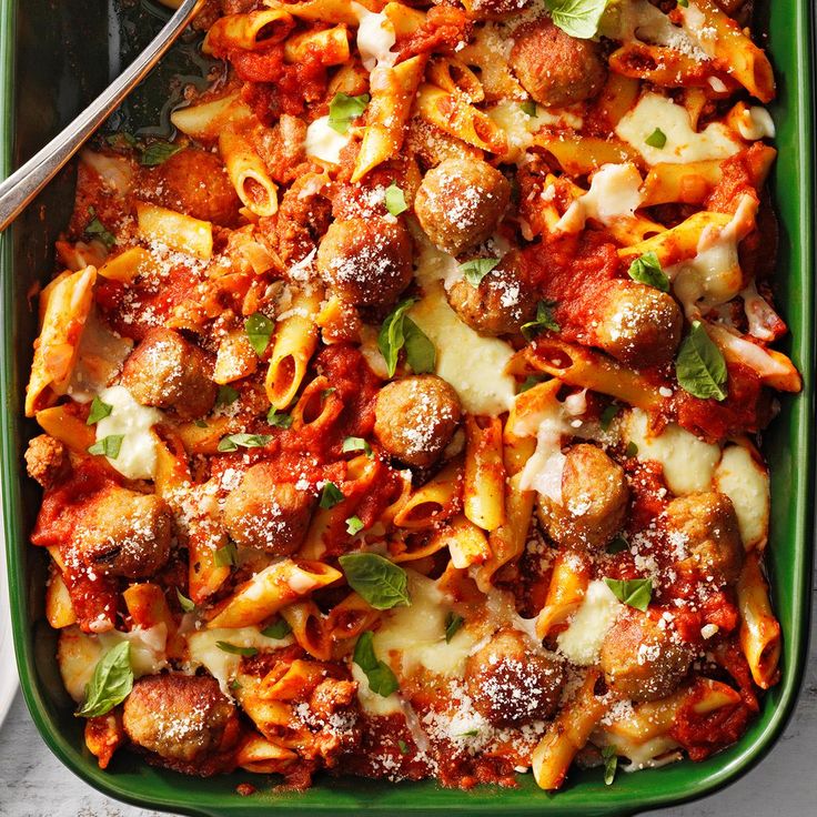 a green casserole dish filled with pasta, meatballs and sauce on a table