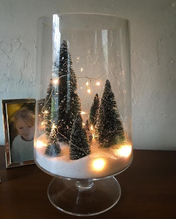 a glass vase filled with christmas trees on top of a table next to a photo