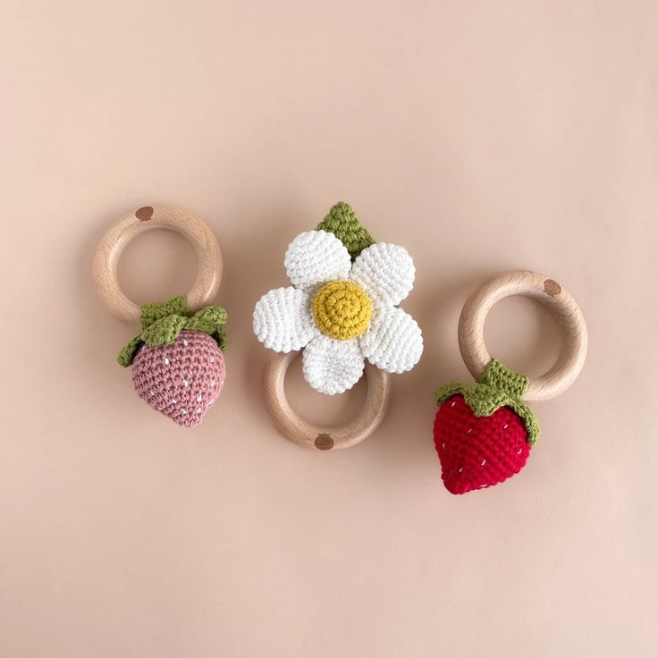 three crocheted strawberries and two wooden rings on a pink background with a flower