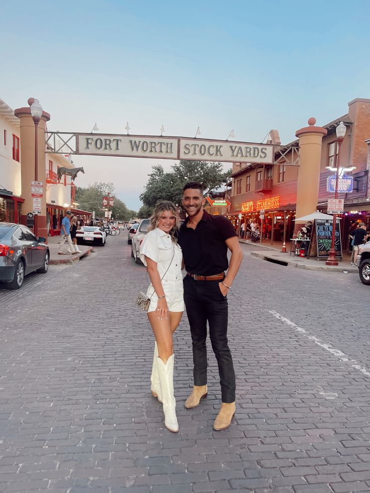 a man and woman standing in front of a foot worth stock yards sign on a brick road