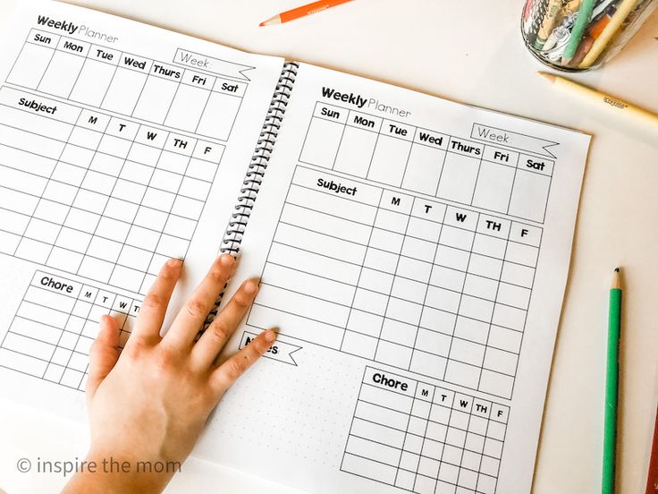 a person's hand is on top of a workbook with pencils and crayons