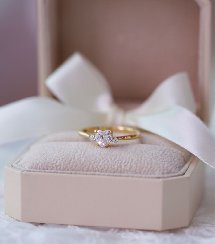 an engagement ring in a box with a white ribbon around it and a bow on the side