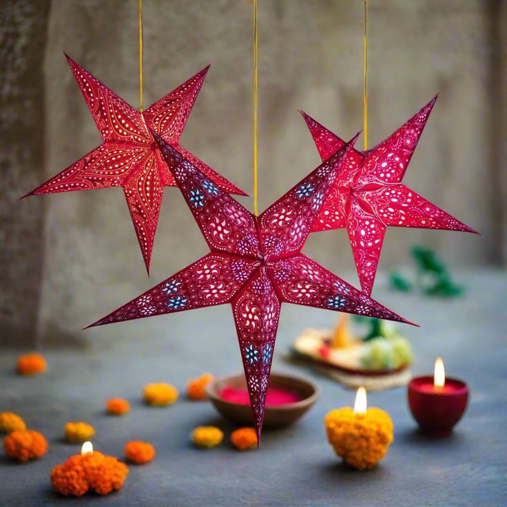 three red paper stars hanging from strings next to small bowls with orange flowers and candles